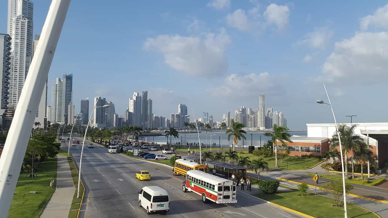 Alt Text: Panama City on a sunny day. You see a beach side street with tall skyscrapers in the background.