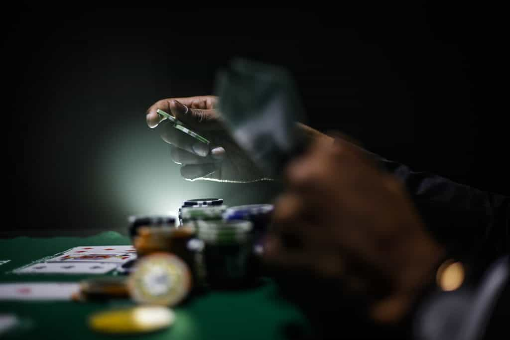 A player lays down cards at a poker table beside stacks of chips.