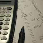 A close-up of a calculator and paper demonstrating lines of expenses.