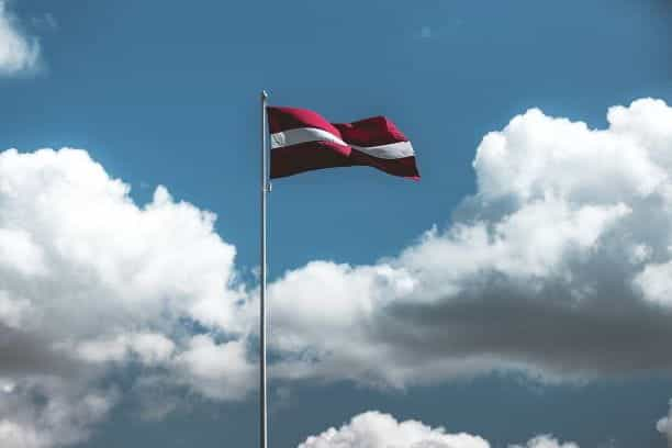 The Latvian flag flying from a flagpole with the sky in the background.