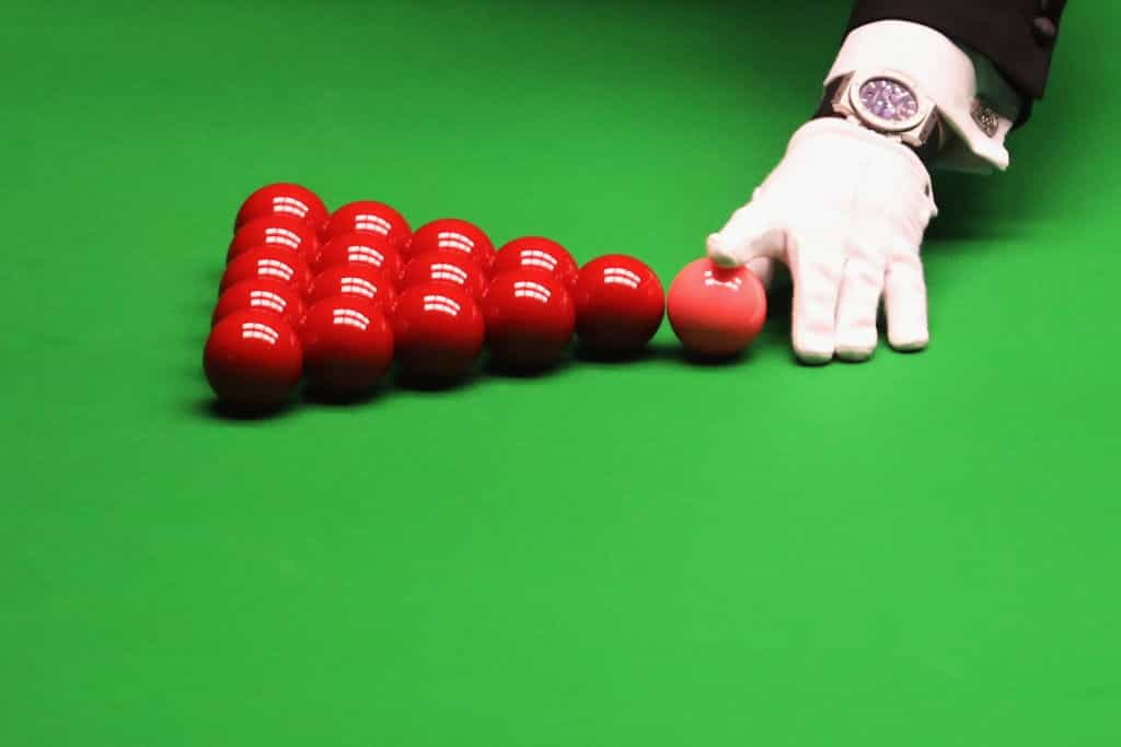 The referee, wearing a white glove, racking up the red balls ahead of a frame of snooker.