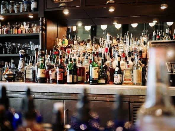 The wall behind a bar, filled with rows and rows of alcohol in bottles.