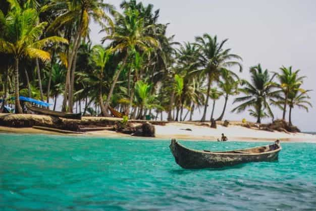 A canoe on the ocean in Panama, with a white sand beach and palm trees in the background.