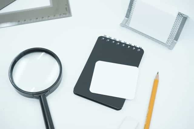 A notepad, pencil, magnifying glass and other detective paraphernalia sit on a white desk.