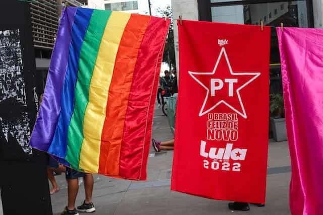 A rainbow flag, a red flag for Lula from the Worker’s Party and a pink flag hang in a row.