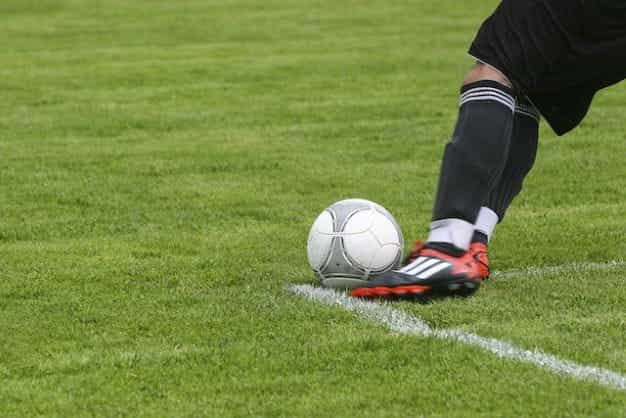 A footballer kicking a ball on a grass pitch.