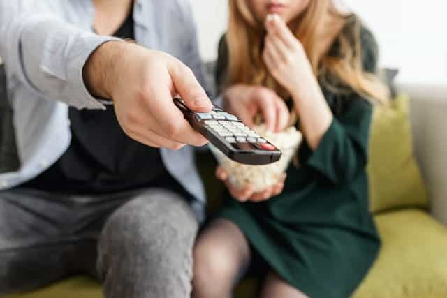 Two people watching TV, pointing a remote control.