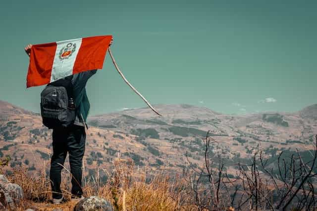 A man carries a Peruvian flag behind his back on a mountain.