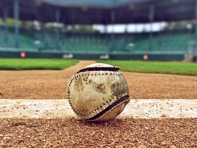 A worn-out baseball sitting in the dirt of a baseball pitch in a baseball stadium before game time.