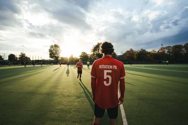 Men stand around a sporting field in jerseys.