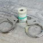 A pair of silver handcuffs sit beside a rolled up wad of cash.