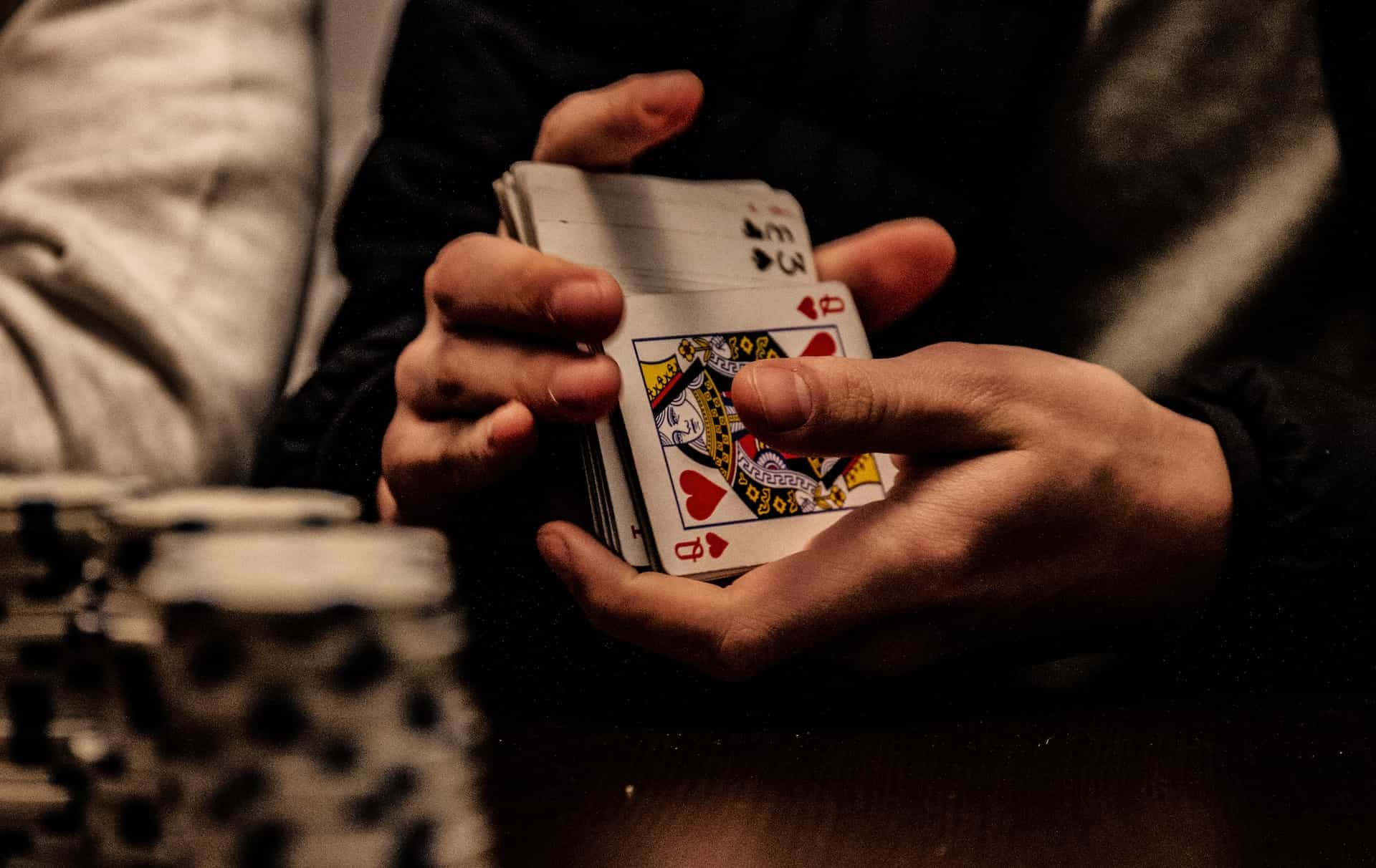 A pair of hands shuffles a deck of playing cards, at a poker table with chips in the foreground.