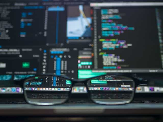 A pair of glasses placed in on the surface of a laptop, the screen of which is displaying several lines of code and text.