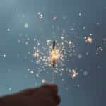 A hand holds a sparkler light emitting sparks.