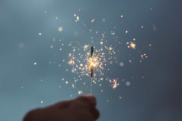 A hand holds a sparkler light emitting sparks.