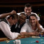 Four men sat in casino playing roulette while having fun and looking happy.